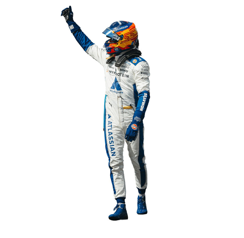 F1 driver Carlos Sainz  in a white 2025 United States GP F1 Racing Suit with blue and orange accents, raising his right hand. Explicit Pro