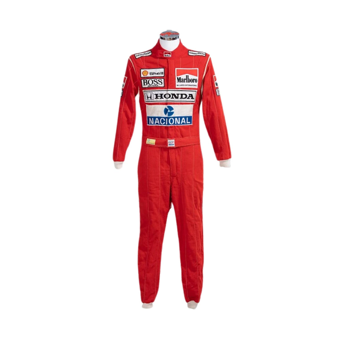 Front view of Ayrton Senna’s 1988 Stand21 F1 racing suit in bright red with white panels and detailed sponsor patches, worn during his championship-winning season. Main image